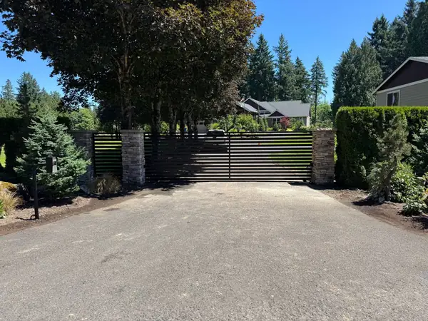 Automatic sliding gate with stone pillars and driveway call box on a sunny day