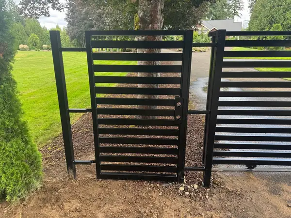 Black horizontal-slat pedestrian gate with lock, matching the main sliding driveway gate