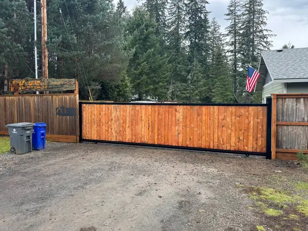 Cedar sliding driveway gate with black steel frame, closed across a gravel driveway