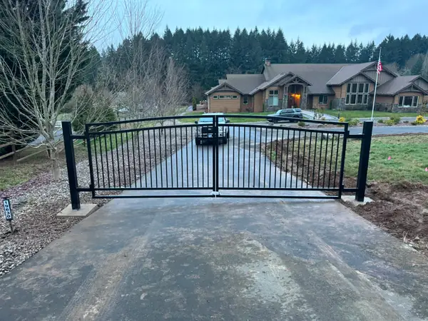Finished black arched double swing driveway gate closed, large home and flag behind