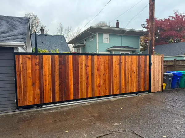 Finished cedar-clad steel-frame sliding driveway gate in alley with keypad