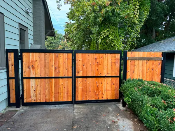 Two-panel cedar swing gate with black steel frames flanked by hedges