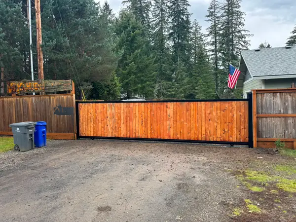 Wide view of finished cedar rolling driveway gate with property sign and flag
